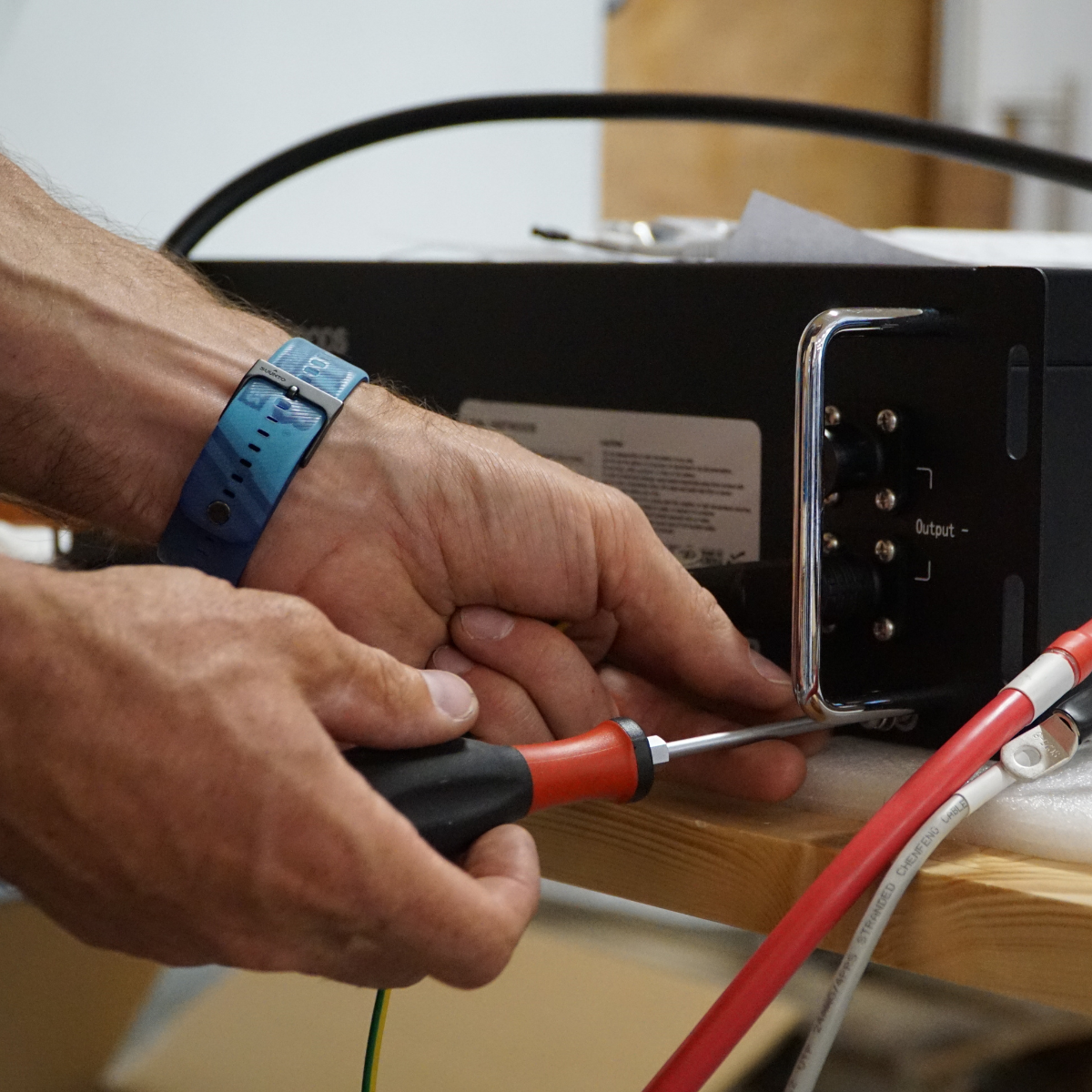 Fachmännische Montage des YOUL ONE: Ein Techniker schließt mit einem Schraubendreher die Verkabelung an das Batteriemodul des Stromspeichers an.